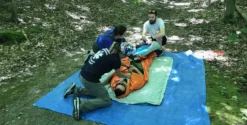Participants prodiguant des soins à une victime sur une bâche en forêt, cours de secourisme en région éloignée.